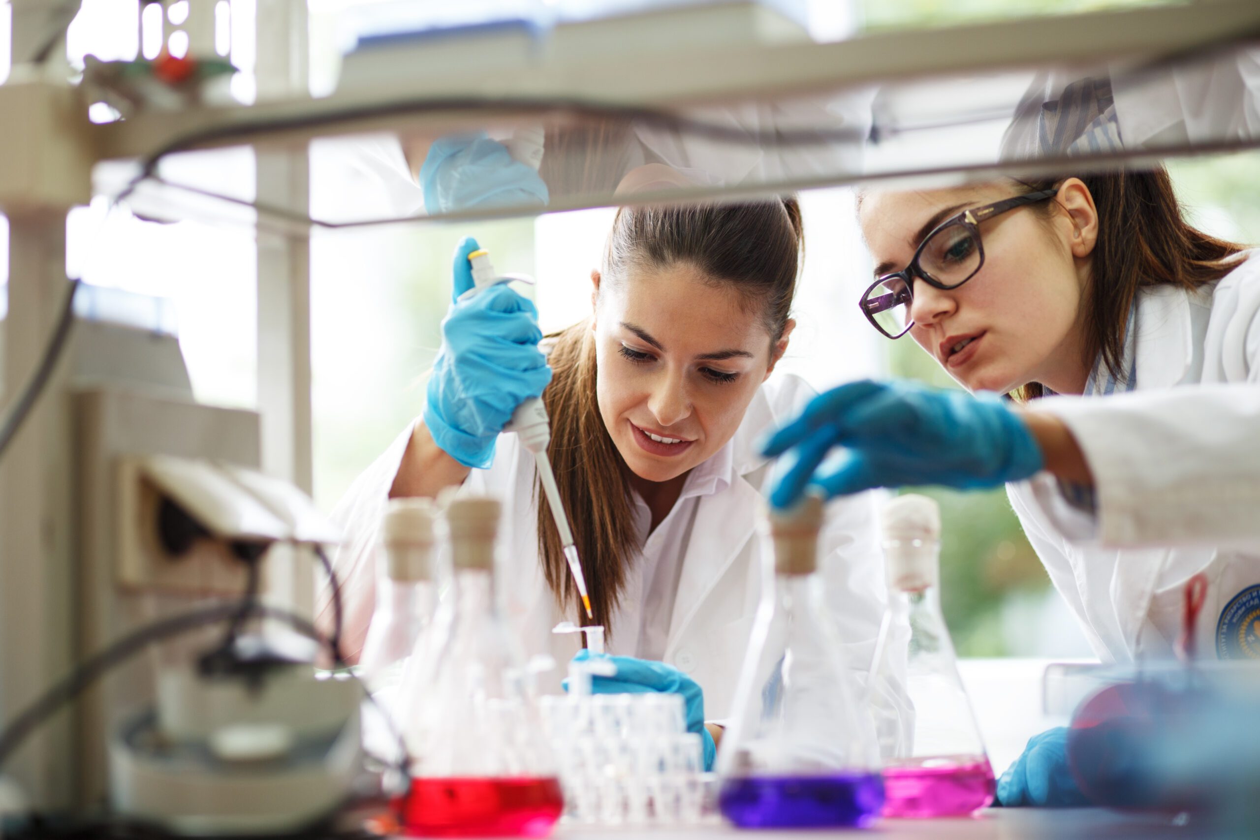 Two dedicated female lab scientists meticulously work together, focusing on chemical research and experiments, advancing scientific knowledge.